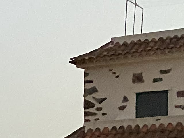 A white house with a tiled roof and an aerial, against an evening sky